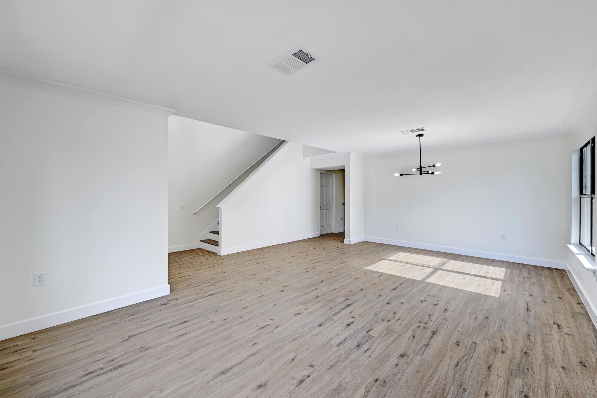 7413 L Marble Ridge Drive Austin, TX 78747 - Photo 3 of 30 Open-concept living area featuring wood-finish flooring, a modern linear chandelier, staircase with white risers, and large windows with black frames