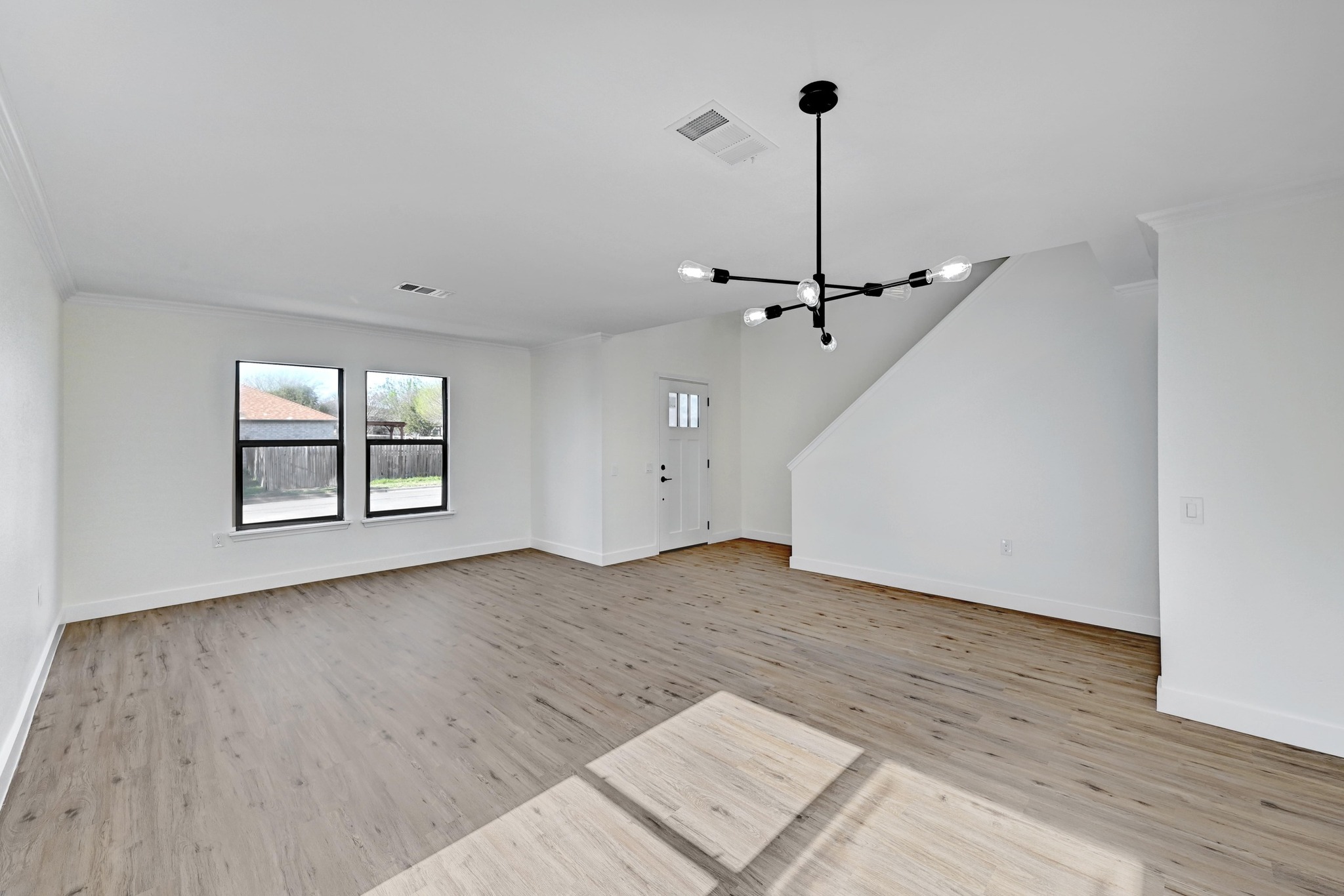 7413 L Marble Ridge Drive Austin, TX 78747 - Photo 4 of 30 Spacious living area featuring wood-finish flooring, a modern black chandelier, crisp white walls, and bright windows with black frames