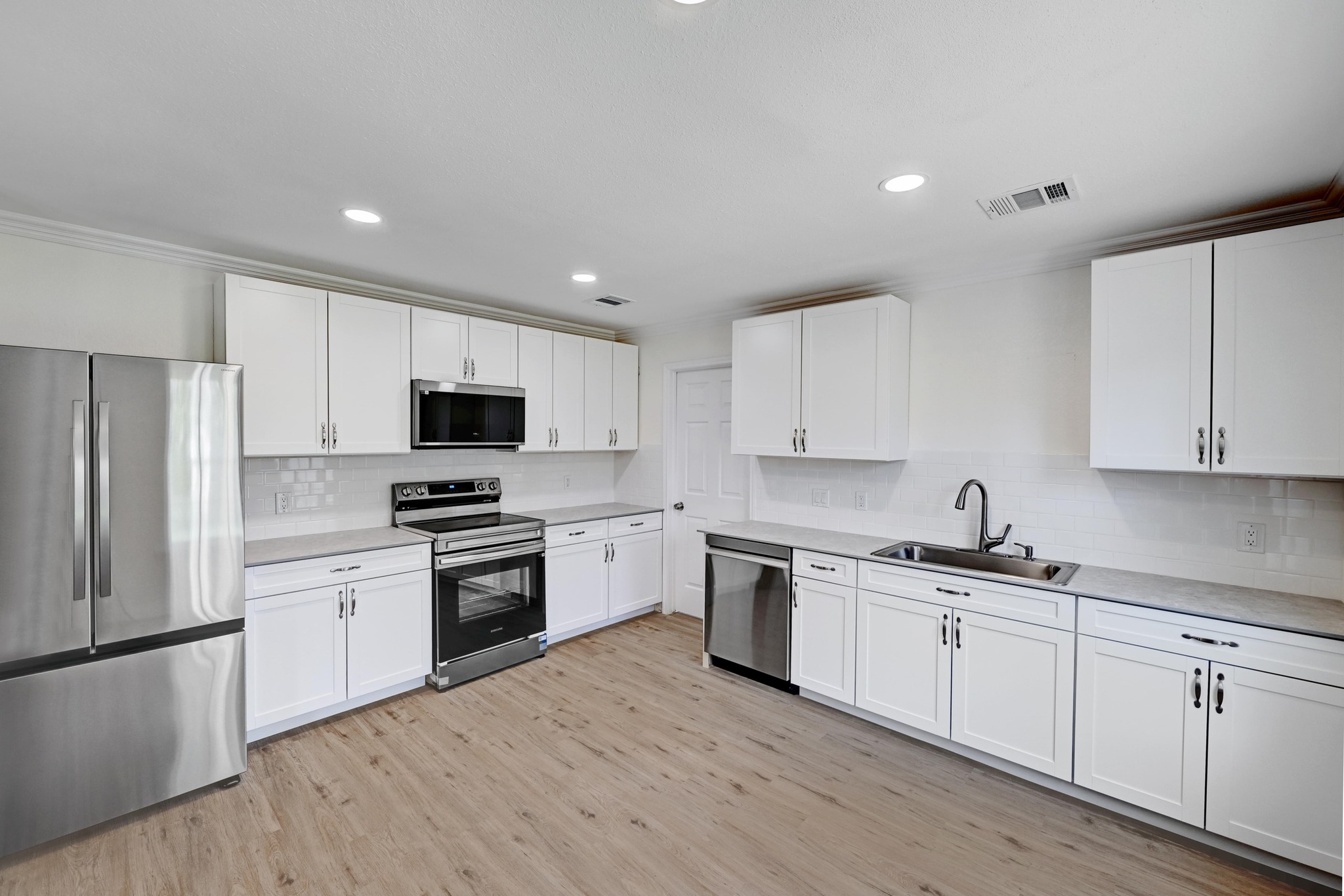 7413 L Marble Ridge Drive Austin, TX 78747 - Photo 10 of 30 Bright kitchen featuring white cabinetry, stainless steel appliances, light countertops, subway tile backsplash, and wood-finish flooring