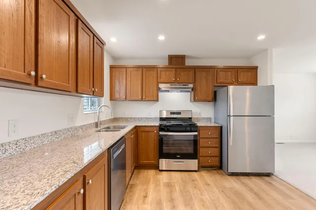 a kitchen with stainless steel appliances granite countertop a refrigerator a stove top oven a sink and dishwasher with wooden floor