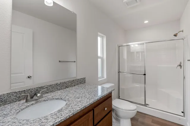 a bathroom with a granite countertop sink a toilet a mirror and shower