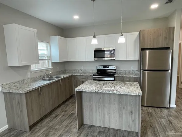 a kitchen with stainless steel appliances granite countertop a refrigerator a sink dishwasher a stove top oven a refrigerator and white cabinets