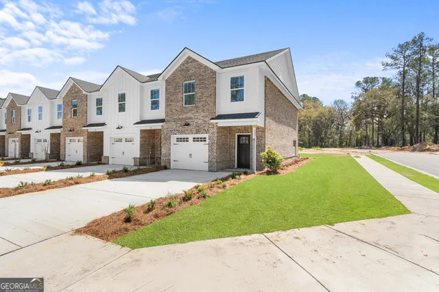 a view of a white house with a yard plants and large tree