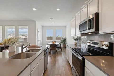 a kitchen with stainless steel appliances a sink a stove top oven a sink a dining table and chairs