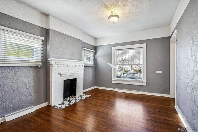 an empty room with wooden floor fireplace and windows
