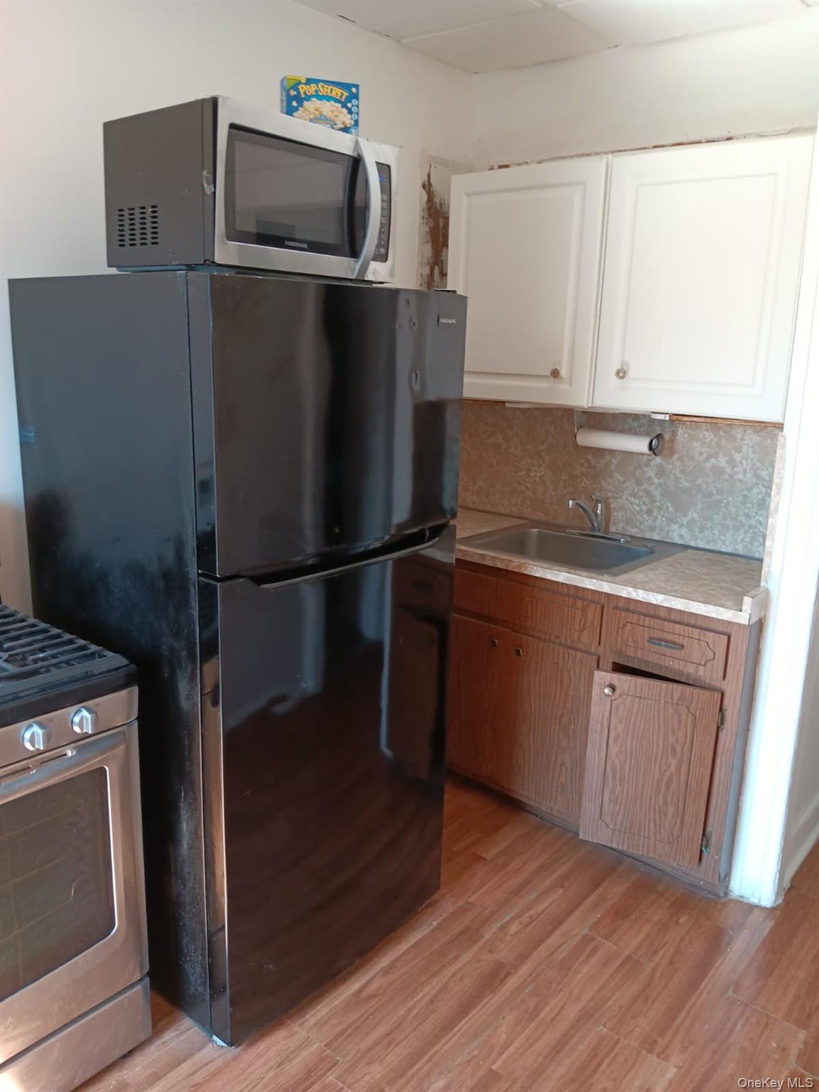 91-08 Sutter Avenue Queens, NY 11417 - Photo 6 of 32 Kitchen featuring appliances with stainless steel finishes, light countertops, light wood-type flooring, tasteful backsplash, and white cabinets