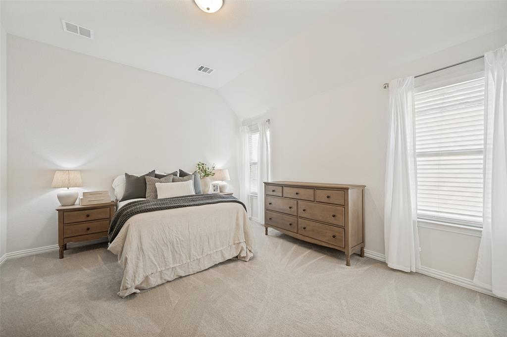8440 Colburn The Colony, TX 75056 - Photo 19 of 34 Spacious upstairs secondary bedroom featuring vaulted ceilings, plush carpet, and large windows that provide abundant natural light. Complete with a walk-in closet and private ensuite bathroom, this comfortable retreat is perfect for family members or guests seeking both space and privacy.
