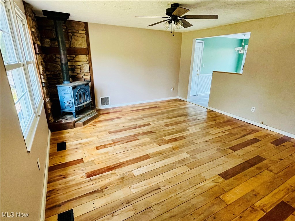 1747 Sterling Road Madison, OH 44057 - Photo 2 of 40 Unfurnished living room with a textured ceiling, light hardwood / wood-style flooring, ceiling fan, and a wood stove