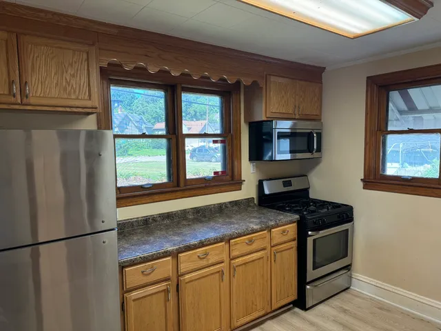 a kitchen with stainless steel appliances granite countertop a refrigerator a stove a sink and a window with wooden floors