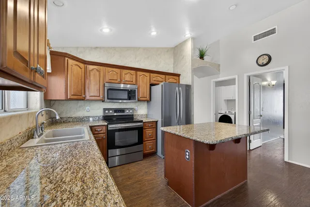 a kitchen with stainless steel appliances granite countertop wooden cabinets a sink dishwasher a refrigerator and a oven with wooden floor