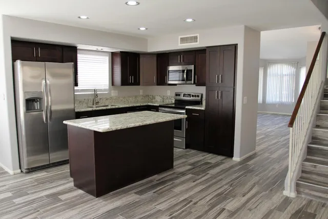 a kitchen with stainless steel appliances granite countertop a refrigerator a sink a stove a microwave and wooden floor