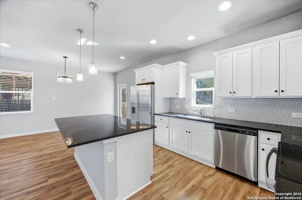 a large kitchen with granite countertop a white stove top oven a chimney wooden floor and cabinets