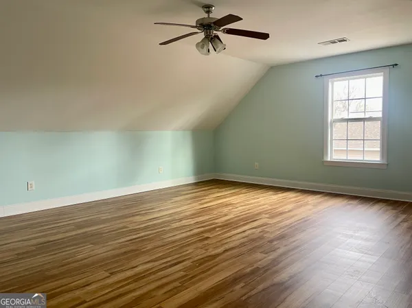 an empty room with wooden floor fan and windows