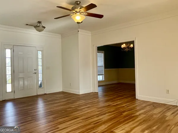 a view of an empty room with wooden floor and a ceiling fan