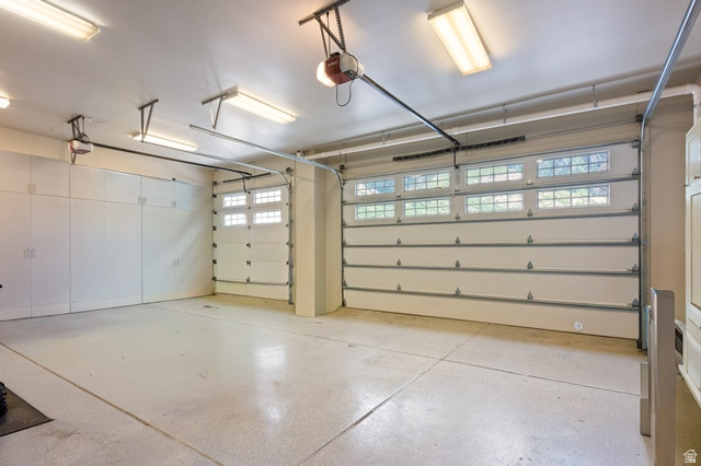 3 Carriagewood Cove, Unit 1088 Sandy, UT 84092 - Photo 64 of 79 Multi-car garage featuring segmented overhead doors with transom windows, full-wall built-in cabinetry, overhead fluorescent lighting, and a sealed concrete floor