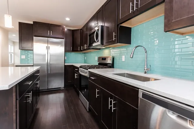 a kitchen with stainless steel appliances granite countertop a sink a stove top oven a refrigerator cabinets and wooden floor