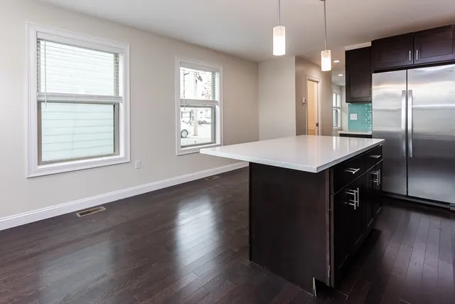 an empty room with wooden floor a kitchen view and windows