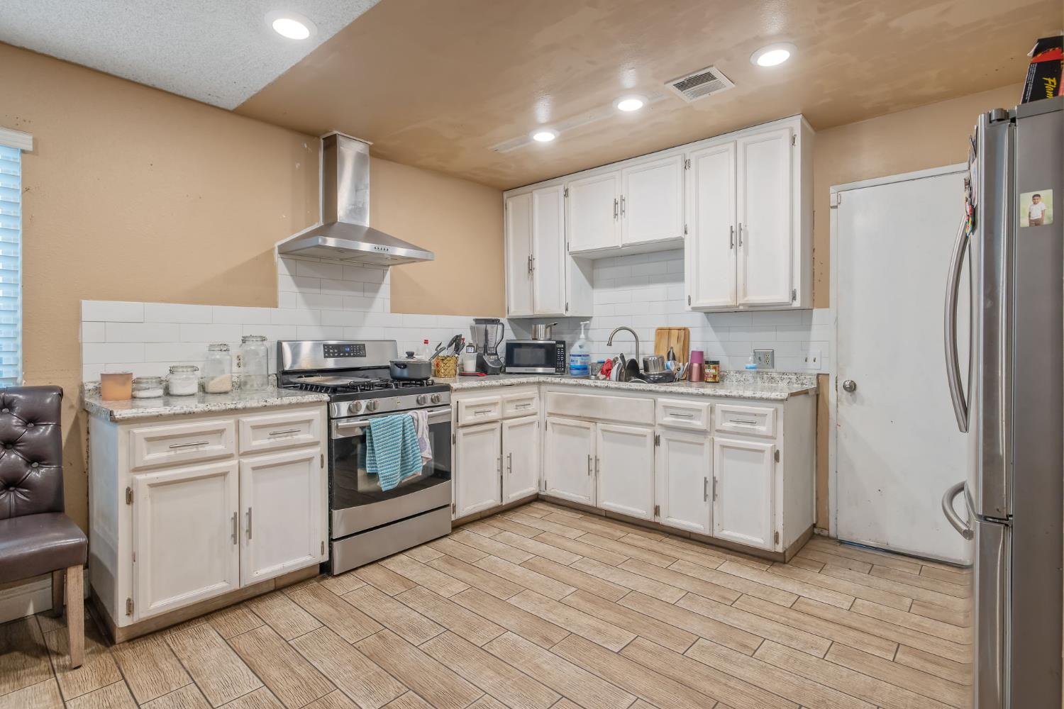 105 West Clark Street Madera, CA 93638 - Photo 12 of 33 a kitchen with stainless steel appliances a sink a stove a refrigerator and white cabinets with wooden floor