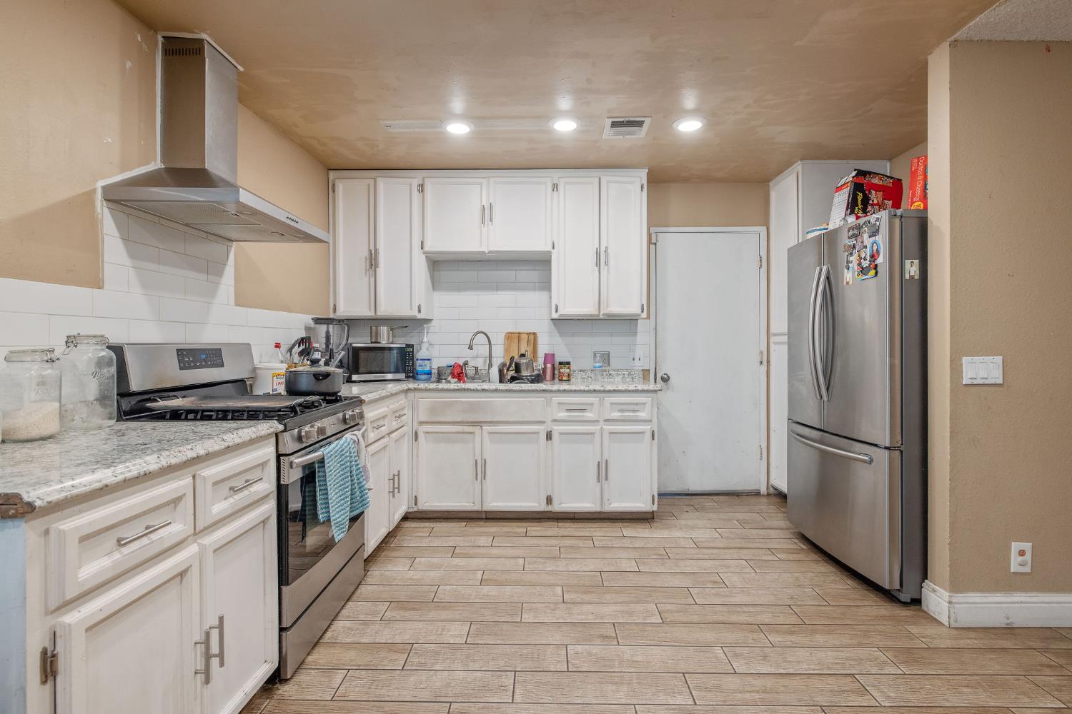 105 West Clark Street Madera, CA 93638 - Photo 13 of 33 a kitchen with granite countertop a refrigerator oven a sink and white cabinets