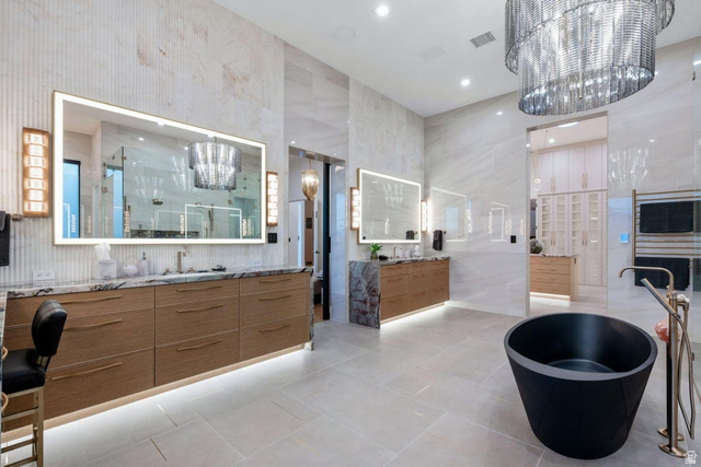2867 East Granite Way St. George, UT 84790 - Photo 32 of 69 Spacious bathroom featuring a freestanding black soaking tub, dual wood-finish vanity cabinets with stone countertops, back-lit mirrors, and large format tile flooring