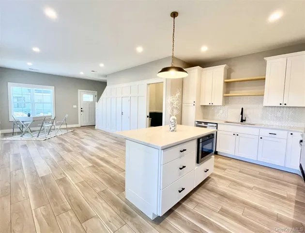 a large kitchen with kitchen island a stove a sink a refrigerator and white cabinets with wooden floor