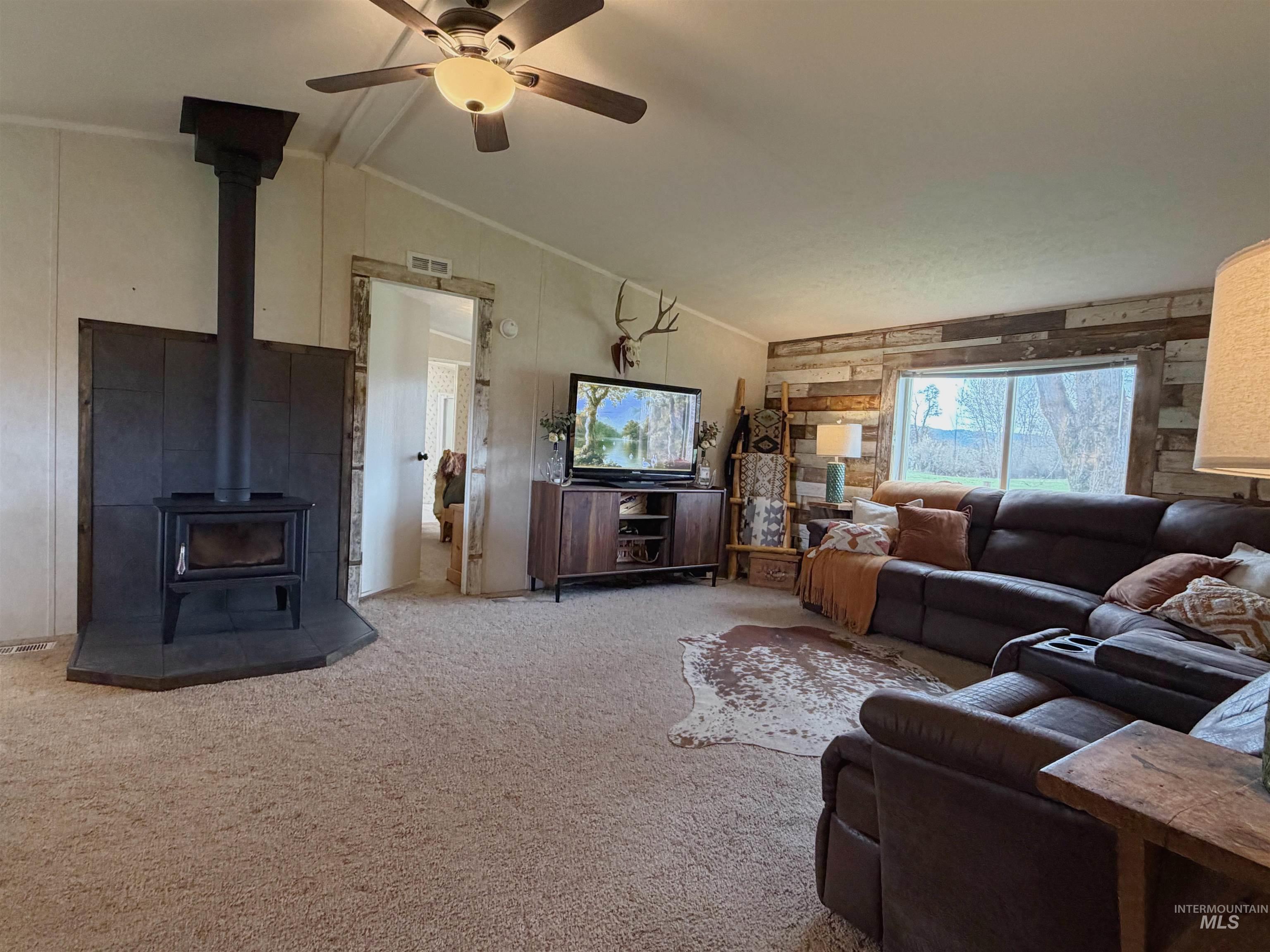 2605 West Frk Road Council, ID 83612 - Photo 14 of 34 Living room featuring ceiling fan, a wood stove, carpet floors, and vaulted ceiling with beams
