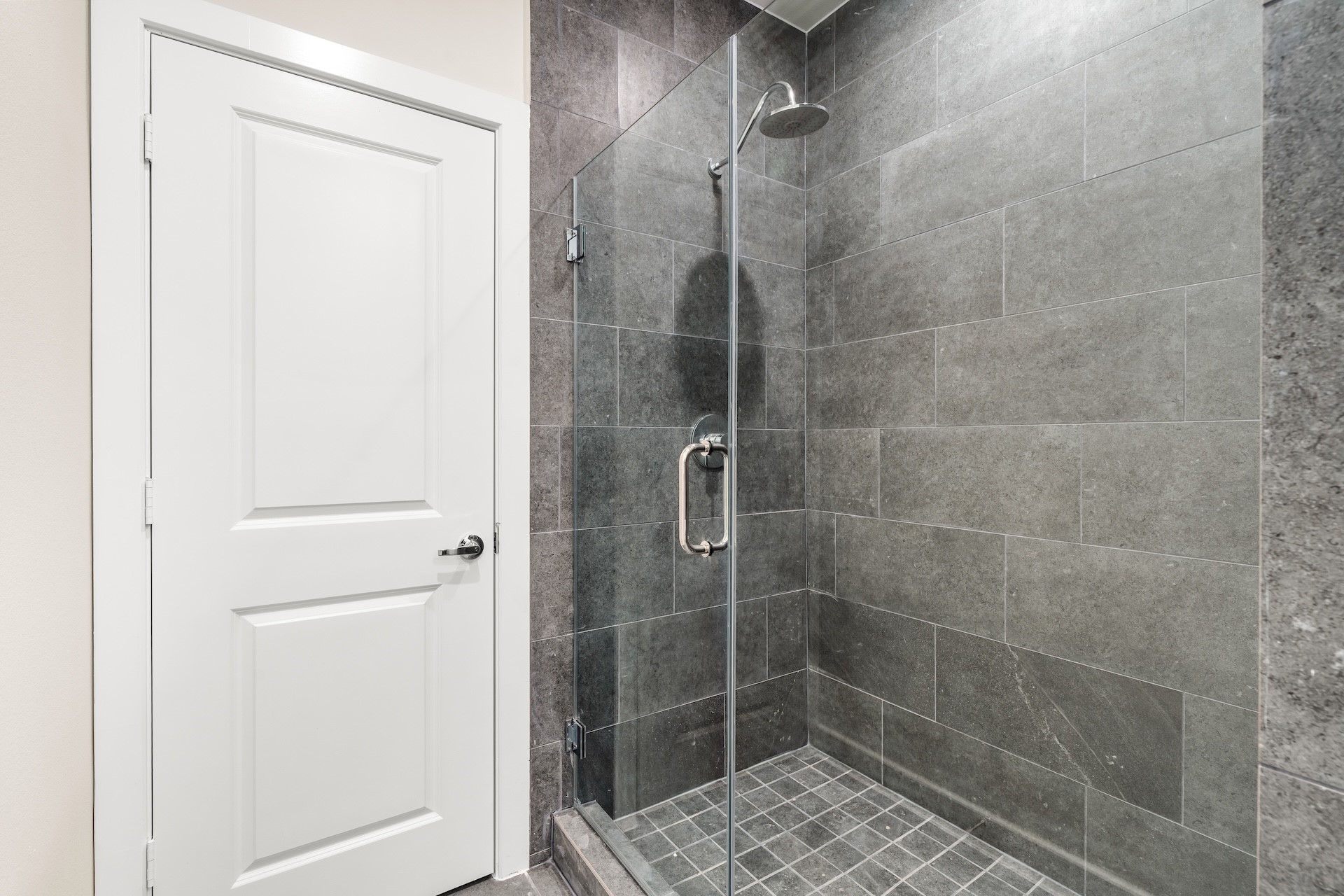 6521 Rena Street Houston, TX 77092 - Photo 16 of 24 Primary ensuite shower — frameless glass enclosure, floor-to-ceiling slate-grey tile surround, matching mosaic tiled basin, and modern chrome rain showerhead.