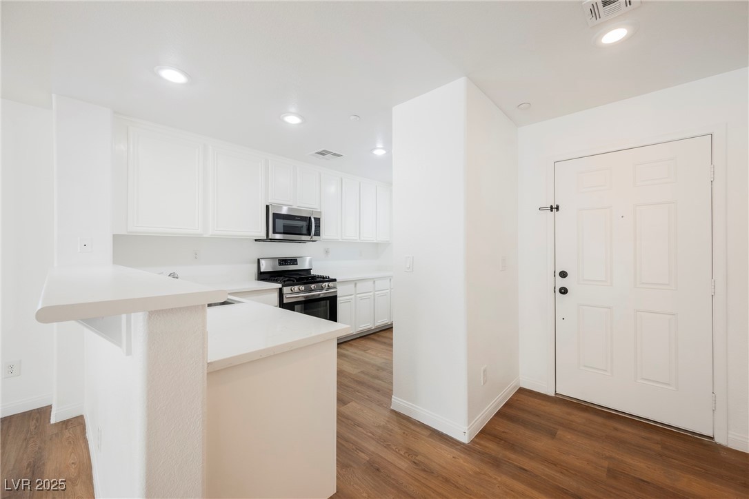 1161 Gecko Road Henderson, NV 89002 - Photo 16 of 54 Kitchen featuring stainless steel appliances, wood finished floors, white cabinetry, light countertops, and recessed lighting