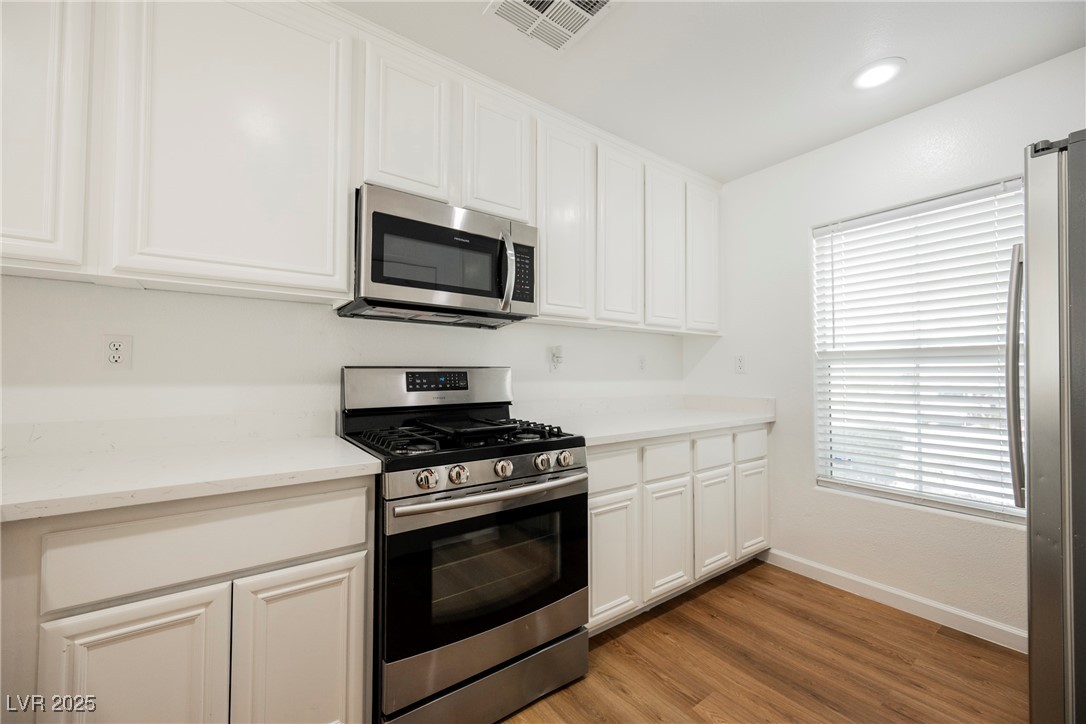 1161 Gecko Road Henderson, NV 89002 - Photo 21 of 54 Kitchen featuring appliances with stainless steel finishes, white cabinetry, light wood-style flooring, and plenty of natural light