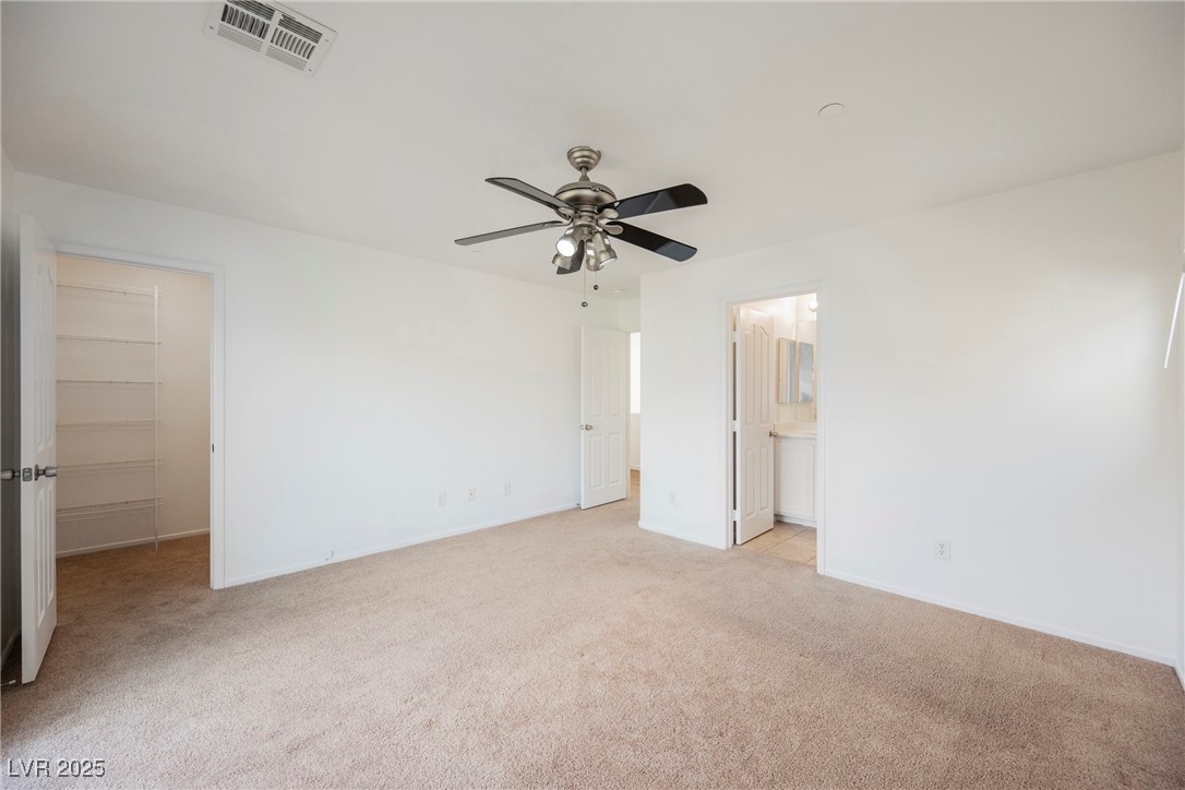 1161 Gecko Road Henderson, NV 89002 - Photo 33 of 54 Unfurnished bedroom featuring light colored carpet, a walk in closet, a closet, connected bathroom, and a ceiling fan