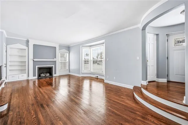 a view of an empty room with wooden floor fireplace and a window