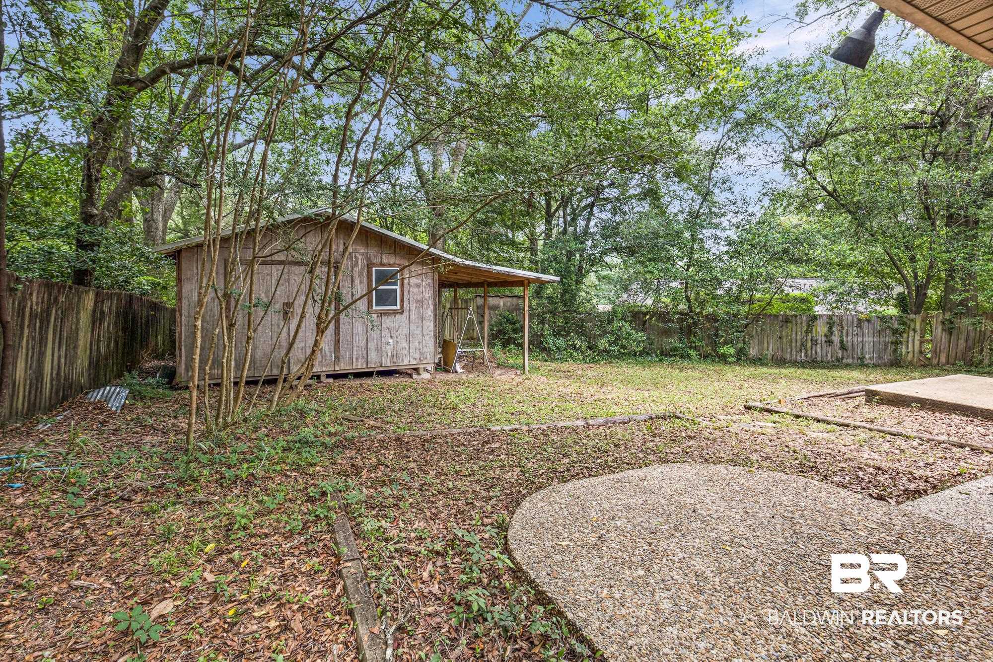 5510 Richmond Road Mobile, AL 36608 - Photo 20 of 21 Expansive backyard featuring a wood-sided storage shed with an attached covered area, a wooden privacy fence, mature trees, and a gravel patio area