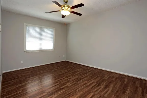 a view of an empty room with wooden floor and a ceiling fan