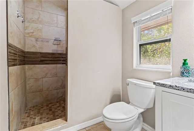 a bathroom with a granite countertop toilet a sink a shower and a window