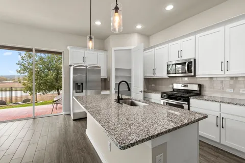 a kitchen with stainless steel appliances kitchen island granite countertop a refrigerator a oven a sink and a wooden floor