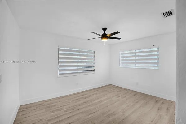 an empty room with wooden floor ceiling fan and windows