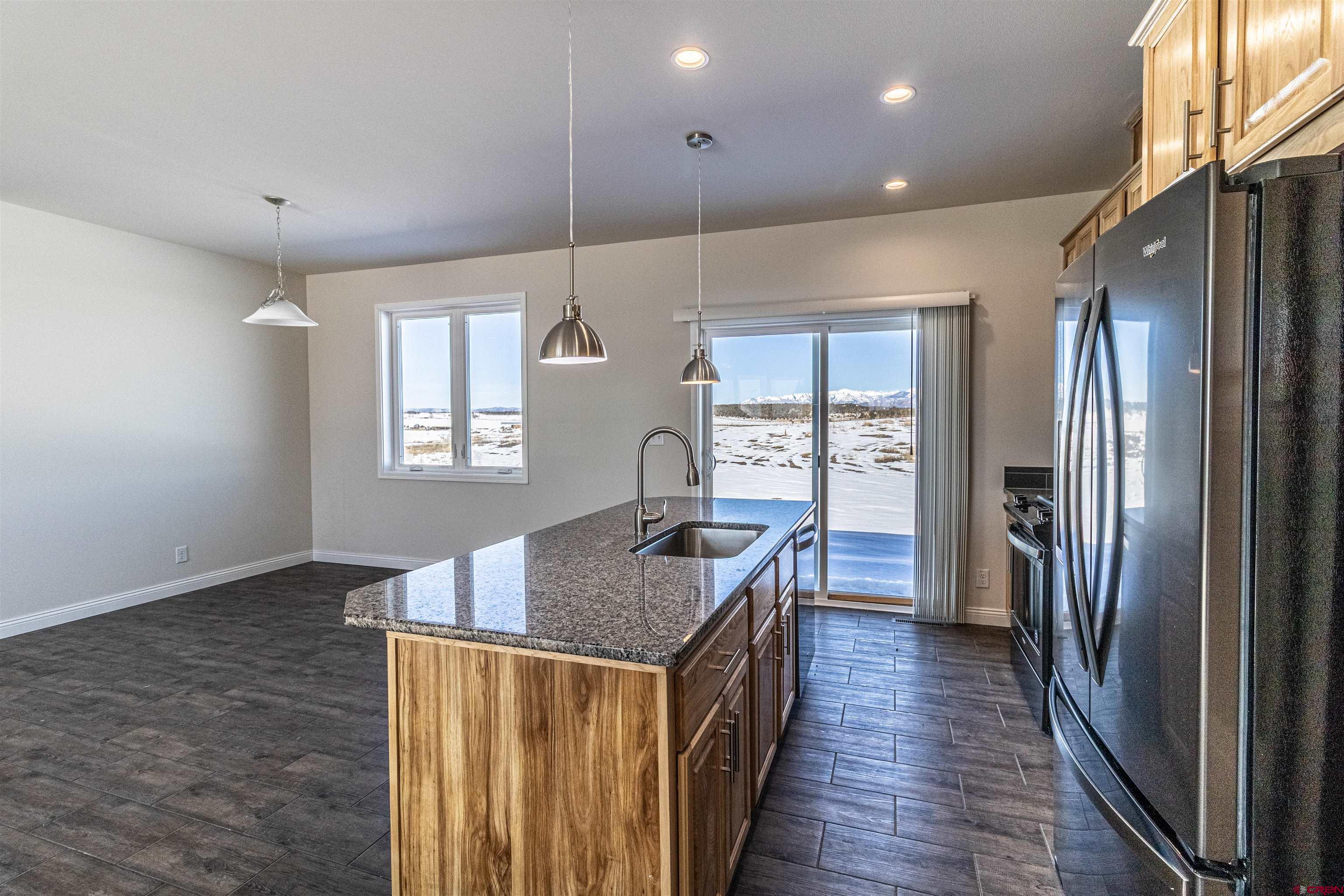 200 Chesterfield Place Ignacio, CO 81137 - Photo 9 of 35 a kitchen with granite countertop a refrigerator a stove top oven a chimney cabinets and wooden floor