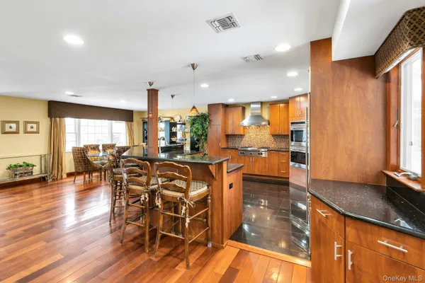 a dining hall with stainless steel appliances granite countertop a stove top oven a dining table and chairs with wooden floor