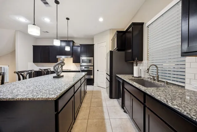 a kitchen with granite countertop kitchen island stainless steel appliances a sink stove and refrigerator
