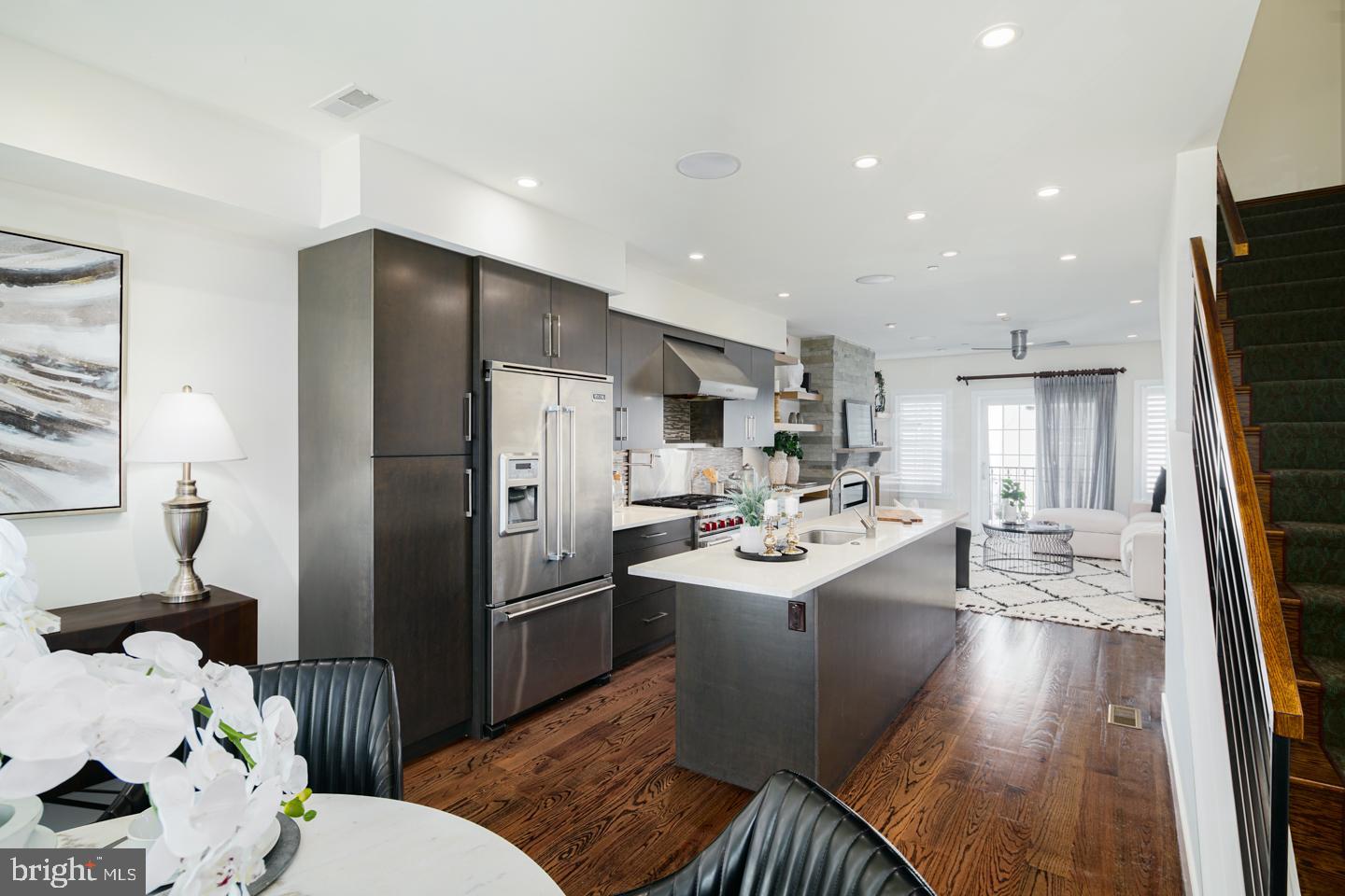 a kitchen with stainless steel appliances a sink a wooden floor and a view of living room