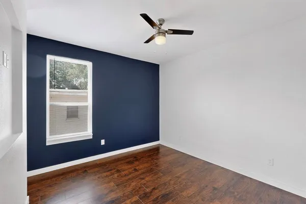 an empty room with wooden floor a ceiling fan and windows