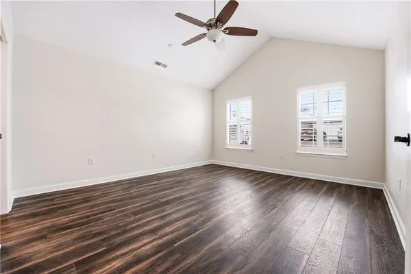 an empty room with wooden floor a ceiling fan and windows