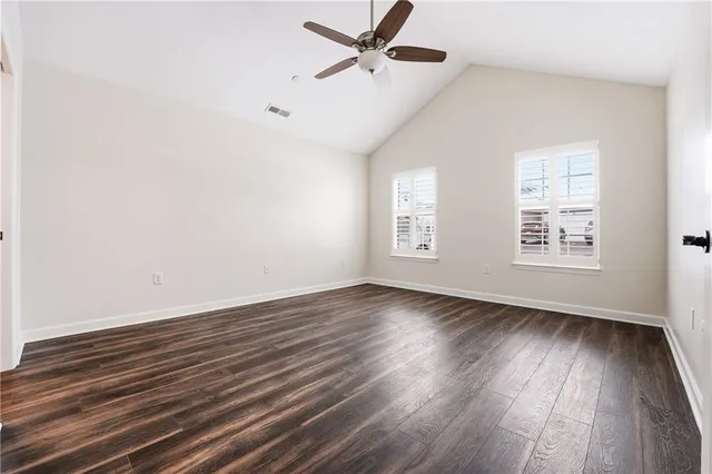 an empty room with wooden floor a ceiling fan and windows