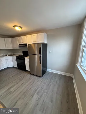 an empty room with wooden floor kitchen view and a window