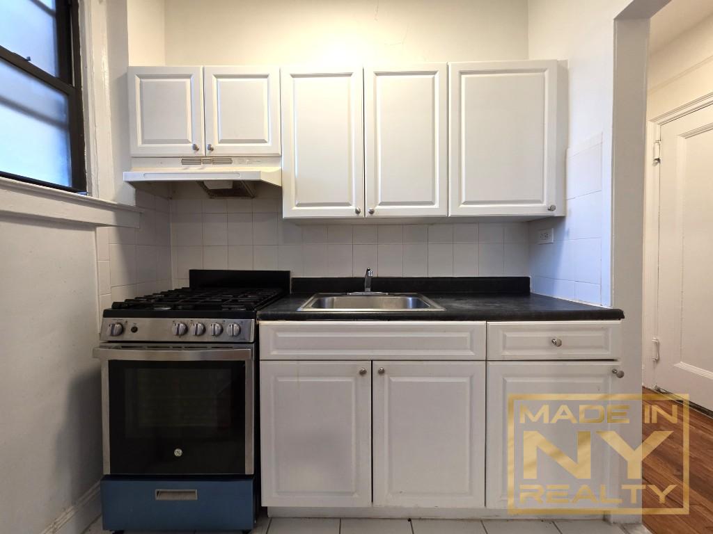 25-74 33rd Street, Unit 5H Queens, NY 11102 - Photo 1 of 4 a kitchen with white cabinets and a stove with wooden floor