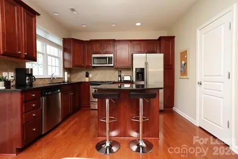 a kitchen with stainless steel appliances granite countertop a refrigerator a sink dishwasher a stove a dining table and chairs with wooden floor