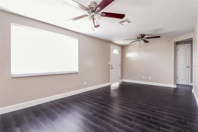 an empty room with wooden floor chandelier fan and windows