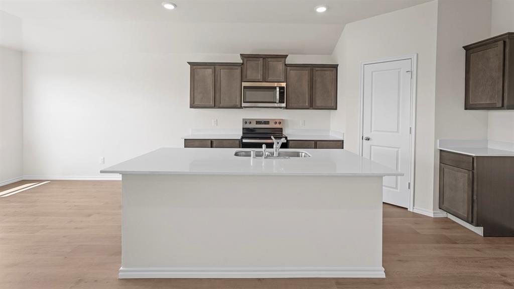 1675 Mantle Road Crandall, TX 75114 - Photo 8 of 27 Kitchen featuring a central island with an undermount sink, white countertops, dark wood-finish cabinetry, stainless steel appliances, and wood-finish flooring