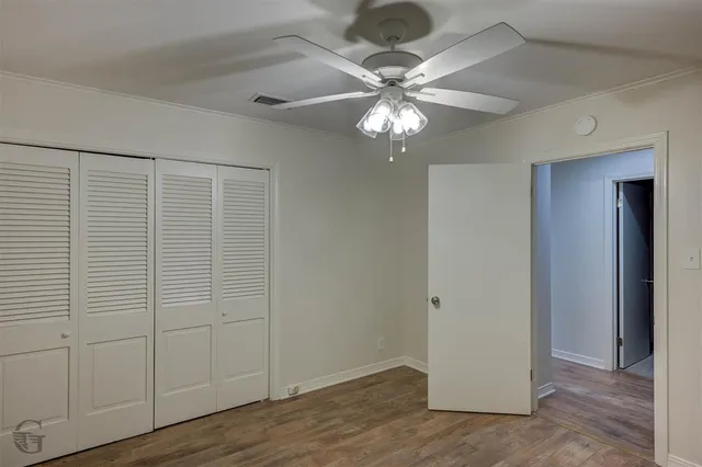 an empty room with wooden floor closet fan and windows