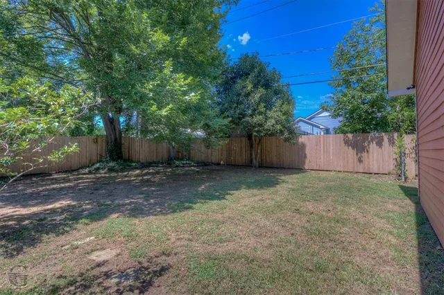 a view of a backyard with large trees and wooden fence
